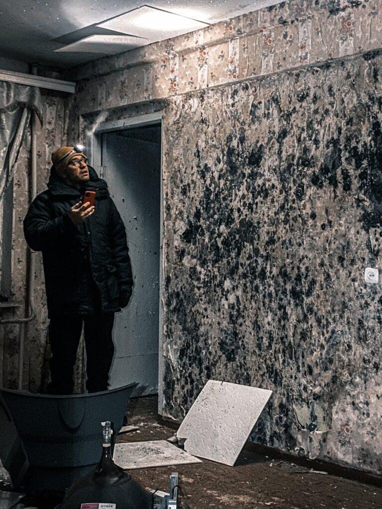 Man with flashlight inspects mold-covered walls in an abandoned building in Vorkuta, Russia.