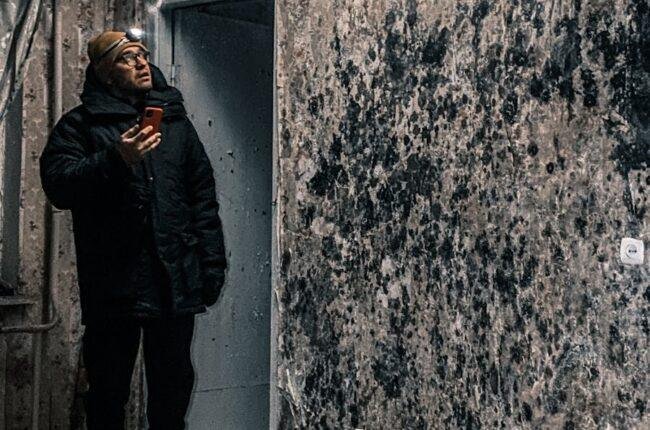 Man with flashlight inspects mold-covered walls in an abandoned building in Vorkuta, Russia.